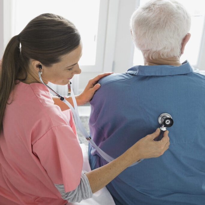 Home care nurse examining man with stethoscope